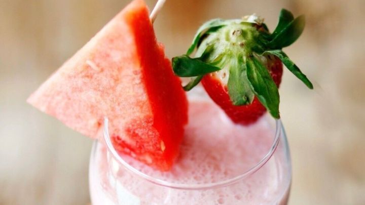 Ein Erdbeershake ist im Glas mit Strohhalm und kleinen Obstst&uuml;cken dekoriert, umgeben von Wassermelonenst&uuml;cken.
