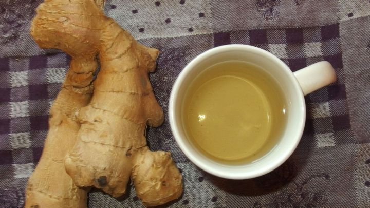Ein St&uuml;ck frischer Ingwer liegt neben einer Tasse Ingwertee auf einem gemusterten Tisch, der die Verdauung f&ouml;rdern soll.
