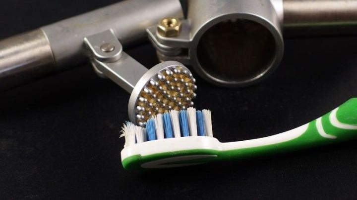 Eine Zahnb&uuml;rste liegt neben einer Knoblauchpresse und reinigt deren Siebteil, auf einem dunklen Untergrund.