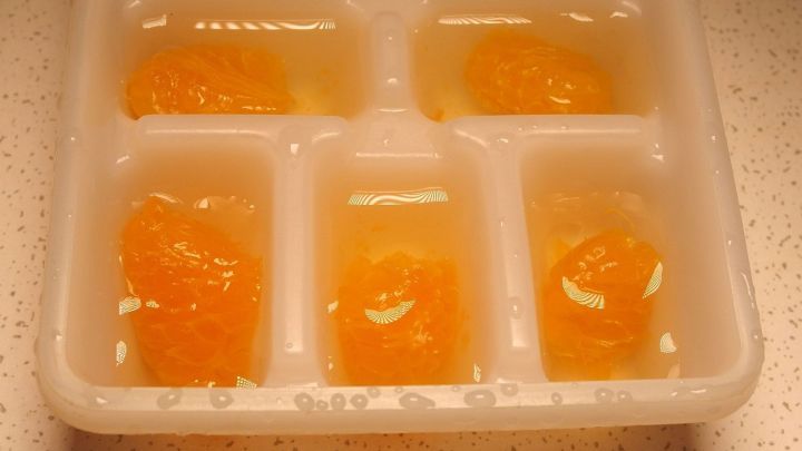 Eisw&uuml;rfel mit Fruchtst&uuml;cken sind in einem Eisw&uuml;rfelfach auf einer hellen Arbeitsfl&auml;che gefroren.