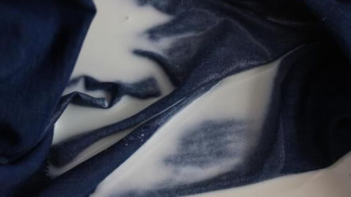 Ein St&uuml;ck dunkler Stoff zeigt einen Fleck, der mit Milch behandelt wurde, um Kugelschreiber- und Tintenflecken zu entfernen.