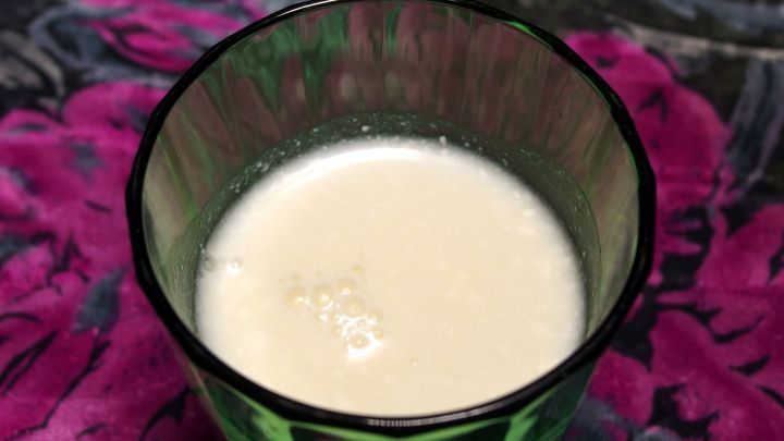Ein Glas Buttermilch steht auf einem bunten, bl&uuml;henden Hintergrund und vermittelt eine erfrischende Wirkung bei Regelschmerzen.