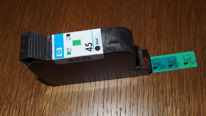 Eine Druckerpatrone liegt auf einem Holztisch, bereit zum Einsetzen, m&ouml;glicherweise mit frischer Tinte, die verschmutzen k&ouml;nnte.