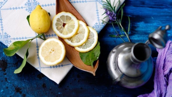 Frische Zitrone und geschnittene Zitrusst&uuml;cke liegen auf einem Holzbrett, umgeben von einem Tisch in blauer Umgebung.