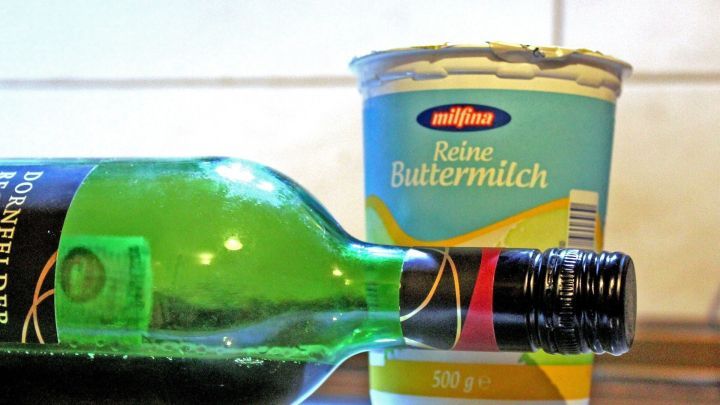 Eine Glasflasche Rotwein liegt schr&auml;g vor einem Becher Buttermilch, der auf einer K&uuml;chenoberfl&auml;che steht.