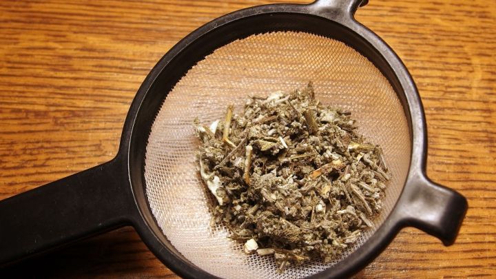 Teebl&auml;tter liegen in einem schwarzen Sieb auf einer Holzoberfl&auml;che, umgeben von Licht und f&uuml;hren zu &bdquo;zarte, reinere Haut&ldquo;.