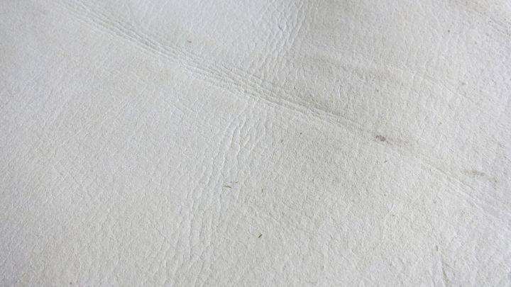 Ein glattes St&uuml;ck wei&szlig;es Kunstleder liegt flach, zeigt eine leichte Textur und kleine Unreinheiten, bereit zum Reinigen.