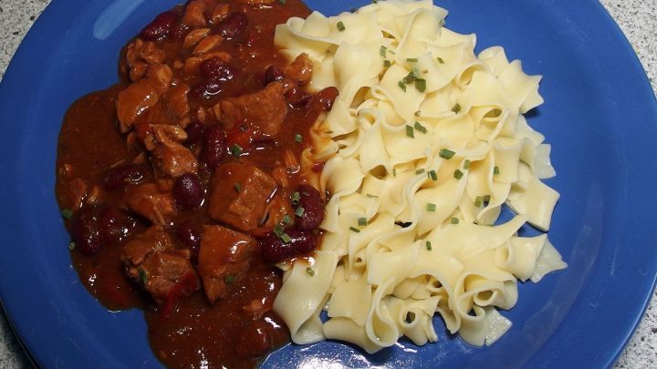 Auf einem blauen Teller liegt ein herzhaftes Gulasch neben Nudeln, ideal f&uuml;r eine einfache und schmackhafte Mahlzeit.