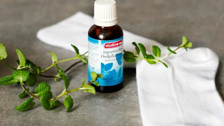 Ein Fl&auml;schchen Minz&ouml;l steht auf einem Tisch, umgeben von frischen Minzbl&auml;ttern und wei&szlig;en Socken, bereit zur Anwendung f&uuml;r geschwollene F&uuml;&szlig;e.