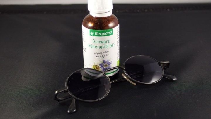 Eine Flasche Schwarzk&uuml;mmel&ouml;l liegt neben einer Sonnenbrille auf einem schwarzen Untergrund, passend zum Thema Sonnenallergie.