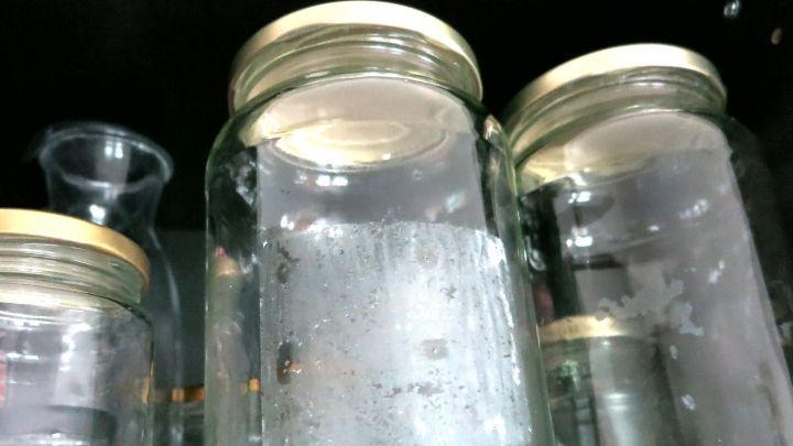 Glasbeh&auml;lter stehen unter Wasser, um Aufkleber zu entfernen. Die Oberfl&auml;chen sind feucht und leicht beschlagen.