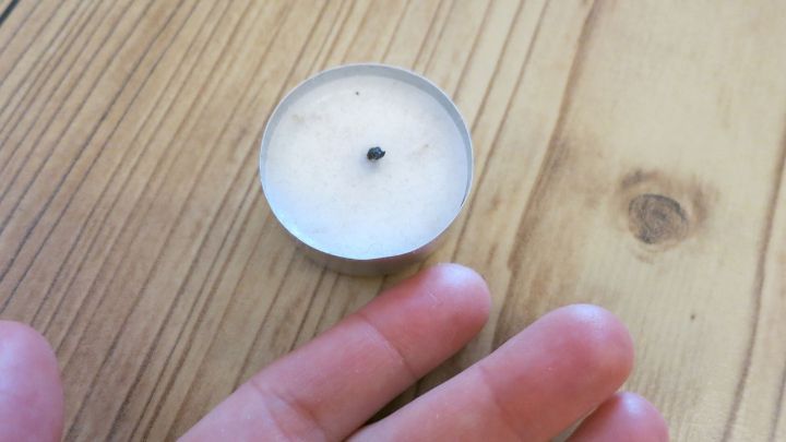 Eine Hand liegt neben einer Teelichtkerze, die bereit ist, Wachs zu verwenden, um einen Stachel aus dem Finger zu entfernen.