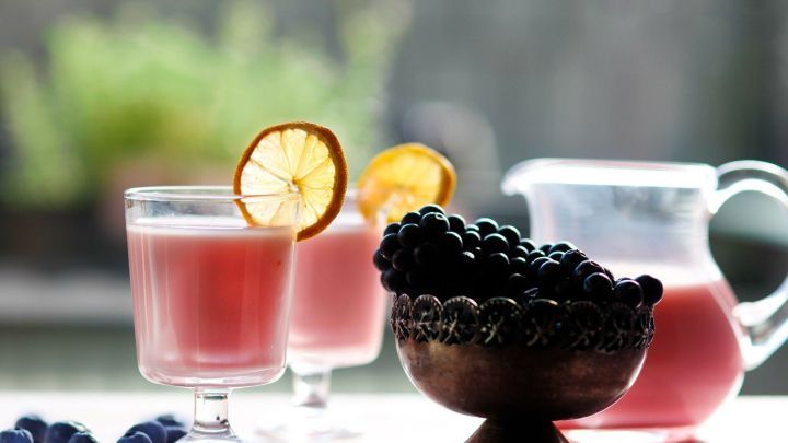 Zwei Gl&auml;ser mit einem erfrischenden Sommerdrink stehen auf einem Tisch, umgeben von frischen Beeren und einer karaffenf&ouml;rmigen Servierkanne.