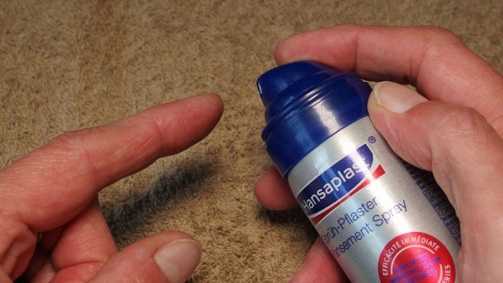 Eine Hand h&auml;lt eine Flasche mit fl&uuml;ssigem Pflaster, w&auml;hrend die andere Hand den Finger mit einer Blase vorbereitet.