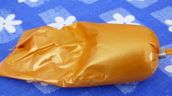 Ein orangefarbenes Wurstpaket liegt auf einem blauen, bl&uuml;tenmusterdekorierten Tischtuch, bereit zur Verwendung.