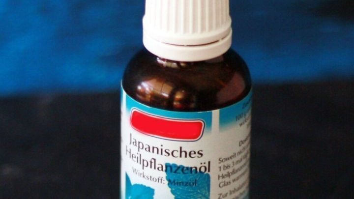 Eine Flasche japanisches Heilpflanzen&ouml;l steht auf dunklem Untergrund. Das Etikett zeigt Minzbl&auml;tter und Text: &bdquo;Japanisches Heilpflanzen&ouml;l, Wirkstoff: Minz&ouml;l&ldquo;.