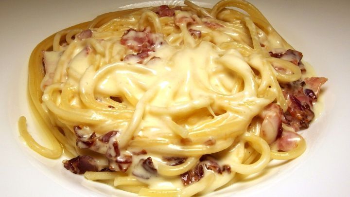 Zarte Spaghetti Carbolio liegen auf einem wei&szlig;en Teller, &uuml;berzogen mit schmelzendem K&auml;se und speckigen St&uuml;ckchen.