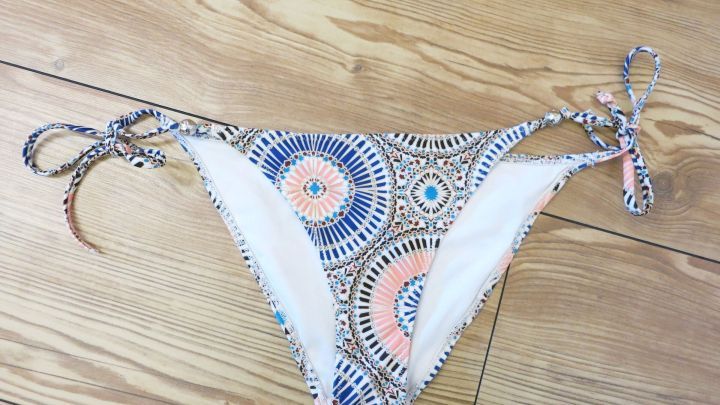 Ein Bikinih&ouml;schen liegt auf einem Holzboden. Es hat ein farbenfrohes, geometrisches Muster und Bindeb&auml;nder.