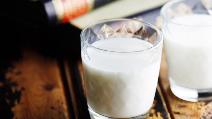 Zwei Gl&auml;ser mit Milch stehen auf einem rustikalen Holztisch, umgeben von einem dunklen Buch.