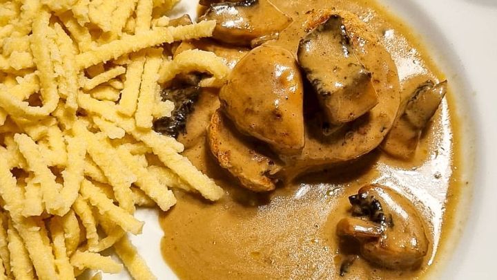 H&auml;hnchenbrust in cremiger Pilzso&szlig;e liegt neben Nudelstreifen auf einem wei&szlig;en Teller, appetitlich angerichtet.