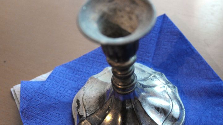 Ein Silberleuchter steht auf einem blauen Tuch, w&auml;hrend er mit Putzstein auf Hochglanz poliert wird.