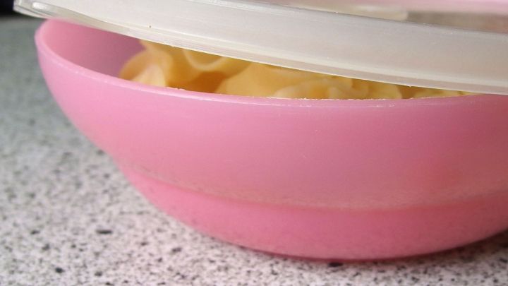 Eine rosa Frischhaltedose mit unpassendem Deckel sitzt schief auf einem K&uuml;chentisch, der Macaroni enth&auml;lt.