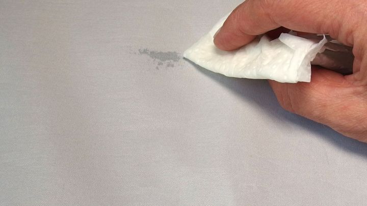 Eine Hand mit einem Tuch rubbelt sanft einen Fettfleck auf einem hellen Stoff.