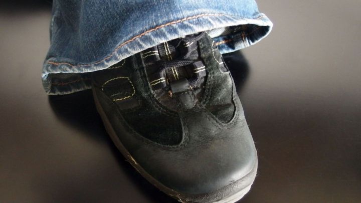 Schwarzer Schuh steht auf einem dunklen Untergrund, w&auml;hrend eine Jeans dar&uuml;ber h&auml;ngt, was eine l&auml;ssige Alltagsszene zeigt.