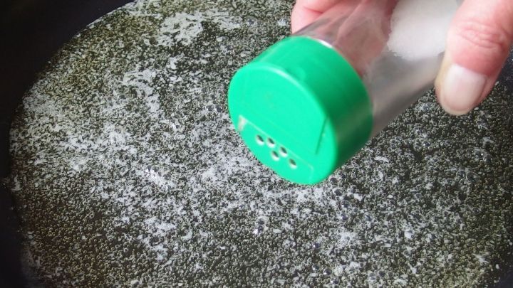 Salzstreuer wird &uuml;ber hei&szlig;e Pfanne geneigt, in der &Ouml;l blubbert.