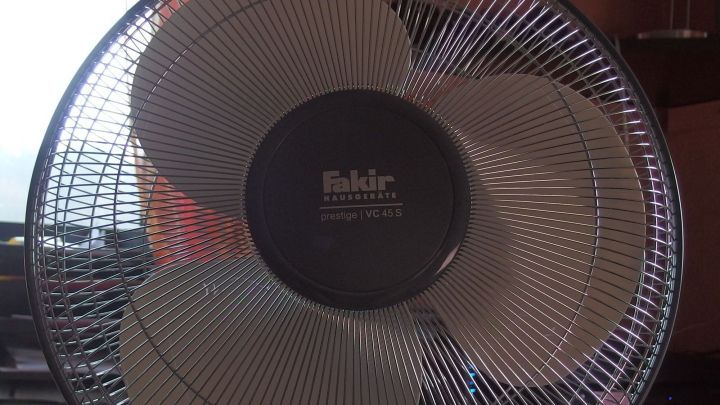 Ein Ventilator dreht sich, w&auml;hrend er frische Luft in einem Raum mit einem Schreibtisch und M&ouml;beln verteilt.