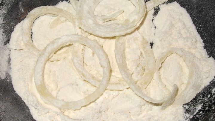 Zwiebelringe liegen in einer Sch&uuml;ssel mit Mehl, bereit zum Frittieren, um knusprig und braun zu werden.