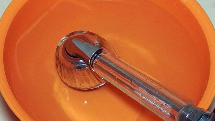 Ein Brausekopf liegt in einem orangefarbenen Eimer mit Wasser, ideal zur Beseitigung von Kalkablagerungen.