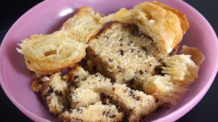 Ein St&uuml;ck &uuml;brig gebliebener Kuchen liegt auf einem pinken Teller, leicht zerbr&ouml;selt und umgeben von Kuchenteilen.