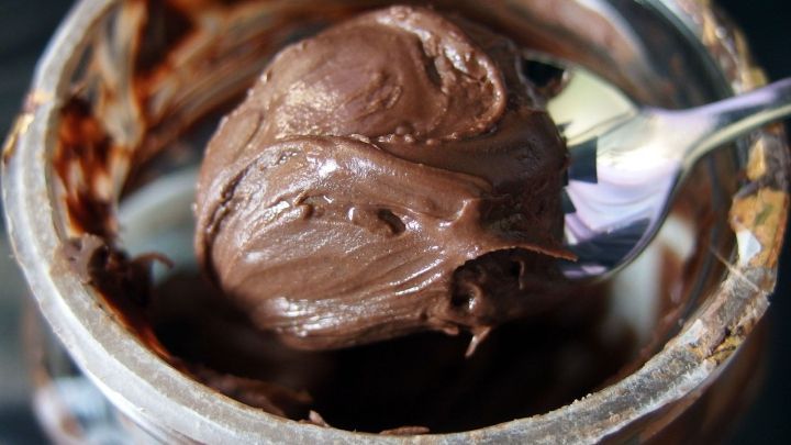 Eine gl&auml;nzende Portion Nutella wird mit einem L&ouml;ffel aus einem Glas entnommen, um sie beim Backen zu verwenden.