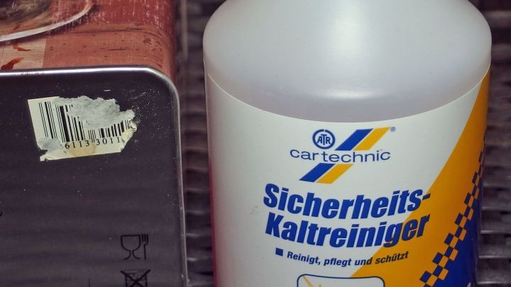 Ein Kaltreiniger steht neben einem Objekt mit einem Aufkleber, der entfernt werden soll, auf einem rauen Untergrund.