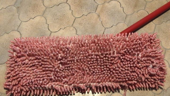 Ein roter Wischmopp liegt auf einem fliesenartigen Boden, bereit zum Waschen, um f&uuml;r die Reinigung verwendet zu werden.