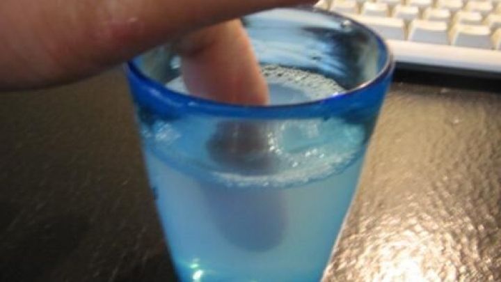 Ein Finger wird in einem Glas mit warmem Seifenwasser eingeweicht, w&auml;hrend eine Tastatur im Hintergrund sichtbar ist.