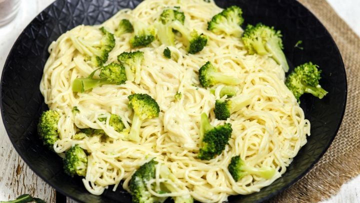 Eine Pfanne mit Spaghetti und Broccoli zeigt das Gericht, umgeben von Oliven&ouml;l und rohen Spaghetti auf einem rustikalen Tisch.