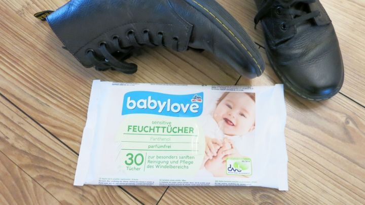 Schwarze Lederschuhe liegen neben einer Packung Babyfeuchtt&uuml;cher auf einem Holzboden, bereit zum Putzen.