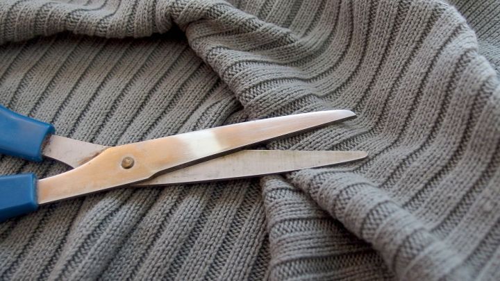 Eine Schere schneidet durch einen grauen, gestreiften Stoff, um hartn&auml;ckige Flecken zu entfernen.