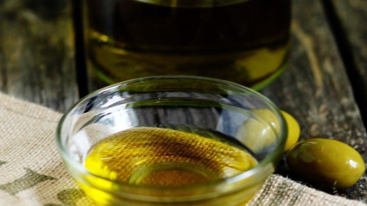 Ein Sch&uuml;sselchen mit Oliven&ouml;l steht auf einem Holztisch, umgeben von einer nat&uuml;rlichen, rustikalen Umgebung.