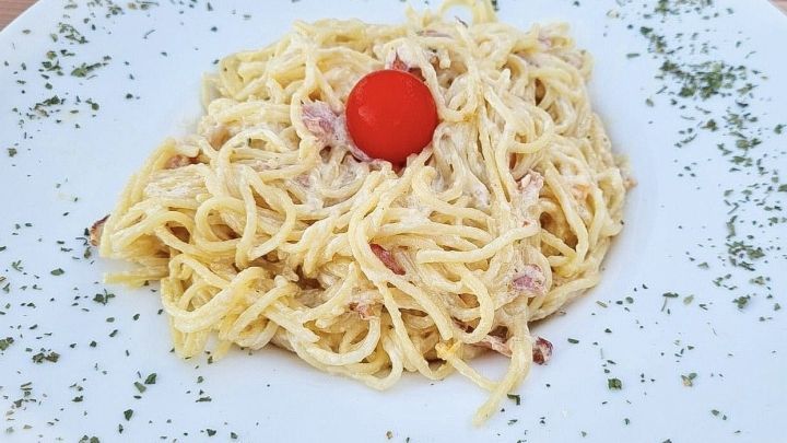 Ein Teller mit Carbonaraso&szlig;e zeigt cremige Spaghetti, dekoriert mit einer Kirschtomate und frischen Kr&auml;utern.