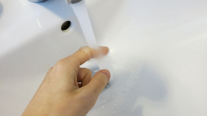 Ein Hand dr&uuml;ckt auf den Wasserhahn, um kaltes Wasser gegen einen Wespenstich in einem Waschbecken flie&szlig;en zu lassen.