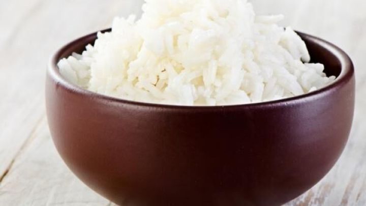 Ein brauner Holzschalen enth&auml;lt dampfenden, flauschigen Reis, bereit zum Servieren nach dem Kochen in der Mikrowelle.