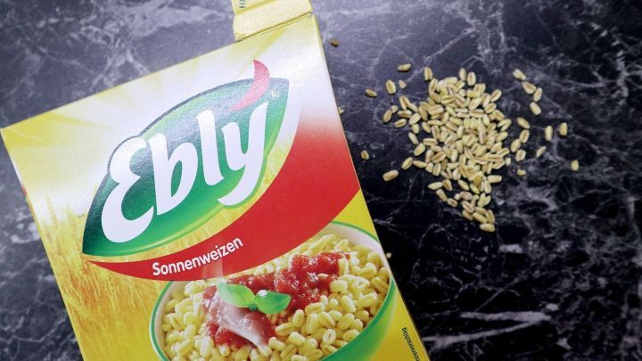 Ein gelbes Paket mit "Ebly" steht auf einer dunklen, marmorierten Oberfl&auml;che, w&auml;hrend kleine, k&ouml;rnige St&uuml;cke daneben liegen.