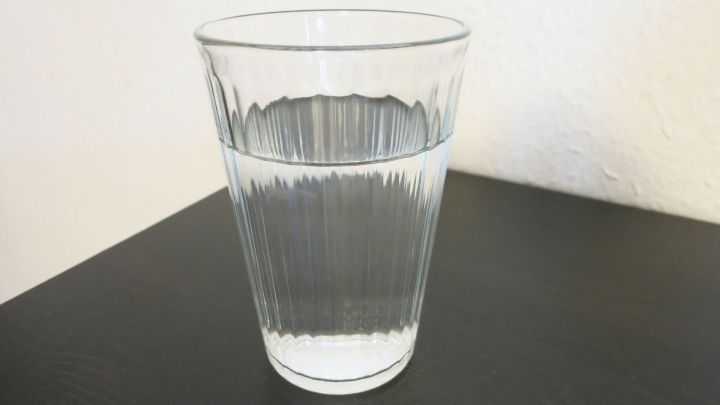 Ein transparentes Glas mit klarem Wasser steht auf einem dunklen Tisch, bereit, den organischen Durst zu stillen.