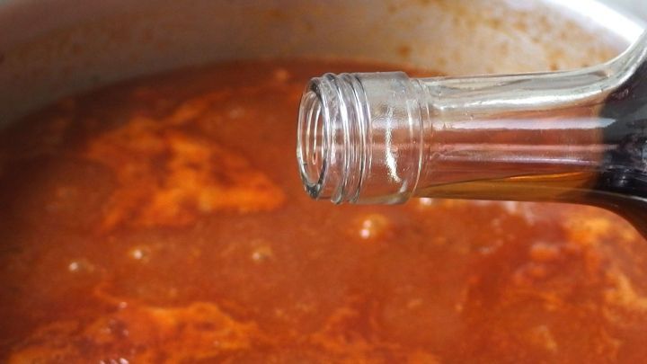 Ein Glas Rotwein wird &uuml;ber einem dampfenden Gulasch in einem Topf eingef&uuml;llt, wodurch das Gericht verfeinert wird.