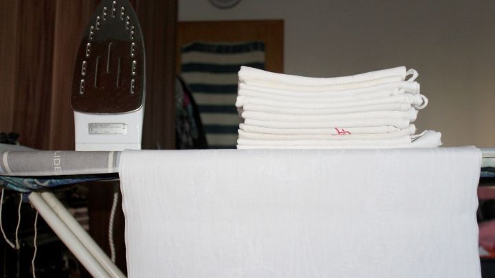 Ein B&uuml;geleisen steht auf einem B&uuml;gelbrett, w&auml;hrend frische, wei&szlig; gefaltete Handt&uuml;cher darauf liegen, bereit zum B&uuml;geln.