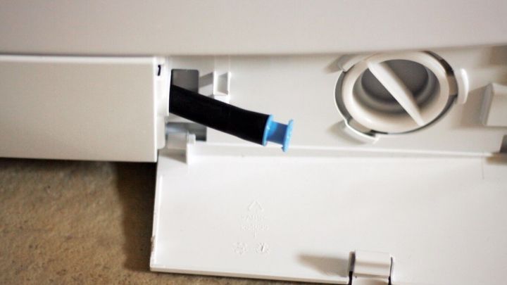 Eine Waschmaschine mit einem ge&ouml;ffneten Zugang, aus dem ein schwarzes Rohr herausragt, um Sand zu entfernen.