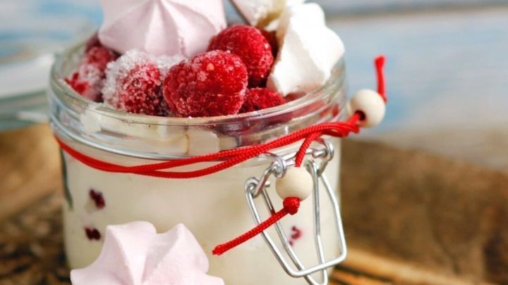 Ein Glas mit einer "coolen" Schichtnachspeise, gef&uuml;llt mit Himbeeren und Baisers, steht auf einem dekorativen Tablett.